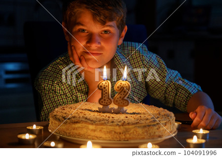 Happy blond little kid boy celebrating his birthday. Preteen child blowing candles on homemade baked cake, indoor. Birthday party for school children, family celebration 104091996