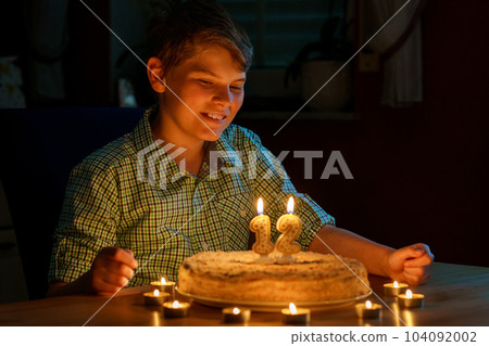 Happy blond little kid boy celebrating his birthday. Preteen child blowing candles on homemade baked cake, indoor. Birthday party for school children, family celebration Happy blond little kid boy celebrating his birthday. Preteen child blowing candles on homemade baked cake, indoor. Birthday party for school children, family celebration 104092002