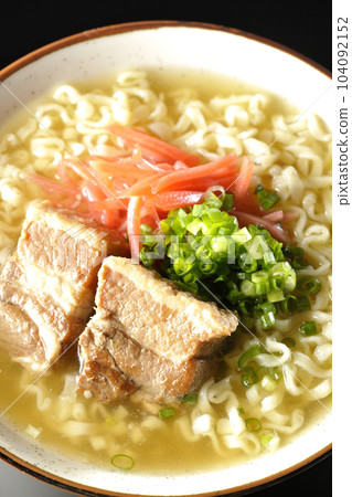 A bird's-eye view of Okinawa soba with pork ribs, plenty of small green onions and pickled ginger on a black background 104092152