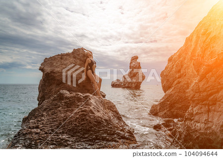 Woman swimsuit sea. Attractive blonde woman in a black swimsuit enjoying the sea air on the seashore around the rocks. Travel and vacation concept. 104094644