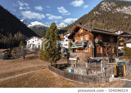 Exterior of houses with sky and trees covered mountains in background at Swiss Alps, Winter holiday travel concept. Small Alpine village. Exterior of houses with sky and trees covered mountains in background at Swiss Alps, Winter holiday travel concept. Small Alpine village. 104096024