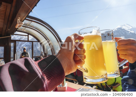 Closeup of tourists toasting beer glasses and celebrating at ski resort during vacation, winter holiday travel concept 104096400