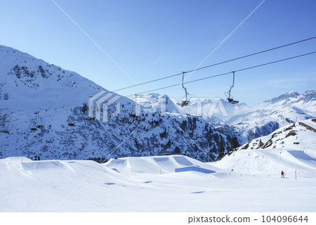 Ski lifts over snow covered landscape with mountains in background on sunny day, winter holiday travel concept 104096644