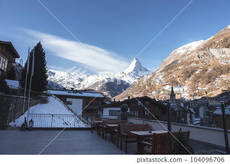 Clock tower and buildings in town in front of beautiful snow covered majestic mountains with sky in background at Zermatt, Switzerland, winter holiday travel concept 104096706