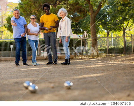 Metal petanque balls against four blurred multiracial senior players in the distance outdoors 104097166