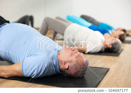 Old man practicing pilates on mat in gym area Old man practicing pilates on mat in gym area 104097177