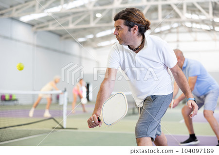 Athletic men playing pickleball tennis on pickleball court indoors Athletic men playing pickleball tennis on pickleball court indoors 104097189