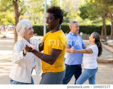 Carefree senior multiracial couples dancing in pairs outdoors during sunny day at park Carefree senior multiracial couples dancing in pairs outdoors during sunny day at park 104097277