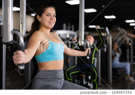 Active young woman training at chest fly machine in gym 104097354