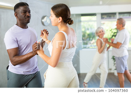 Young woman teaching group of multiethnic mature people social dance Young woman teaching group of multiethnic mature people social dance 104097360