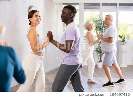 Girl teacher dances pair dance with african male student of fitness class Girl teacher dances pair dance with african male student of fitness class 104097410