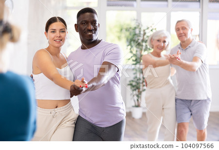 Young woman teaching group of multiethnic mature people social dance 104097566