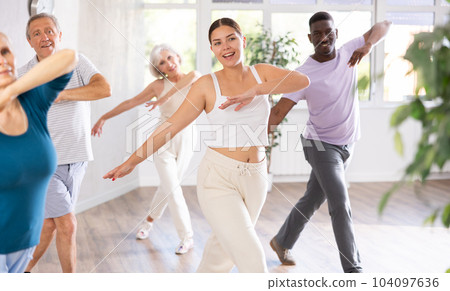 Female instructor teaches mature students of dance class basic movements of hip hop dance Female instructor teaches mature students of dance class basic movements of hip hop dance 104097636