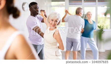 African-American man dances steamy salsa with elderly female companion for fitness classes 104097685
