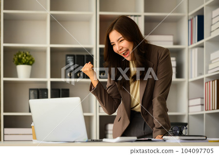 Surprised businesswoman reading good news in email, raising hand in yes gesture celebrating business success 104097705