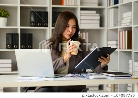 Pretty young woman entrepreneur in luxury suit sitting at modern workplace and reading financial reports Pretty young woman entrepreneur in luxury suit sitting at modern workplace and reading financial reports 104097786