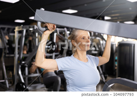 Elderly woman exercising on lat pull down lever machine 104097793
