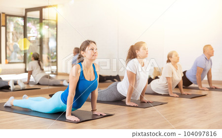 People of different ages performing cobra exercise during group Pilates workout. Active lifestyle and wellness concept People of different ages performing cobra exercise during group Pilates workout. Active lifestyle and wellness concept 104097816