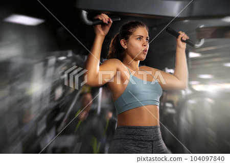 Active young woman training at shoulder press machine in gym 104097840