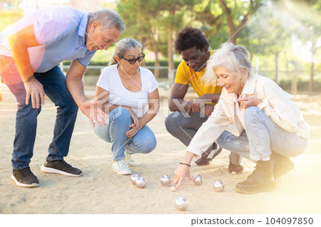 Positive mature diverse percioners comparing the distance of pumped balls after petangue at the sunny afternoon outdoors Positive mature diverse percioners comparing the distance of pumped balls after petangue at the sunny afternoon outdoors 104097850