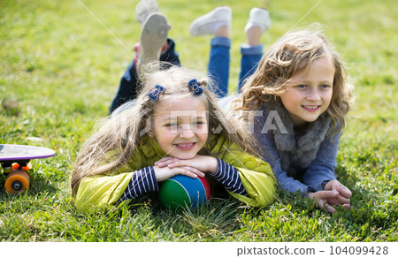 two blonde girl lie on grass in spring 104099428