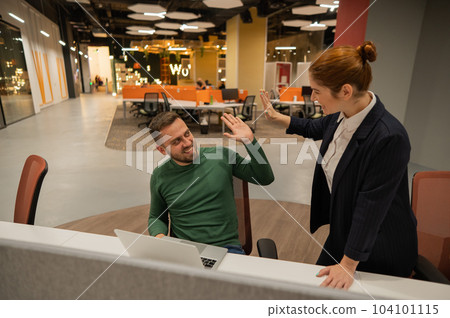 A red-haired Caucasian woman stands at the desktop of a bearded man. The boss approves the work of the subordinate and gives five.  104101115