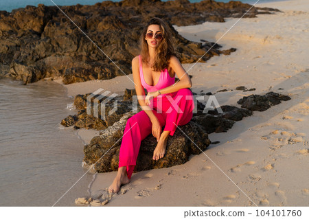Fashion stylish beautiful sensual young woman, slim, in trendy bright pink pants and bodysuit on a tropical beach at sunset posing in sunglasses 104101760