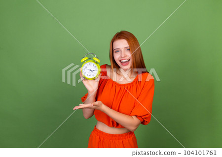 Young red hair woman in casual orange blouse on green background holding alarm clock happy cheerful excited smiling 104101761
