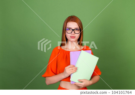 Young red hair woman in casual orange blouse and eye glasses on green background holding notebooks confident smile Young red hair woman in casual orange blouse and eye glasses on green background holding notebooks confident smile 104101764