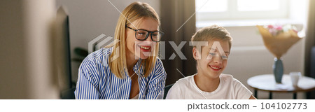 Female babysitter is teaching little boy use laptop application during studying 104102773