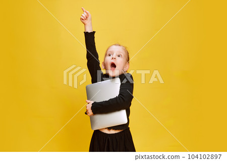 Portrait of smart, preschool little girl, child posing with laptop against yellow studio background. Online education, remote studying and leisure 104102897
