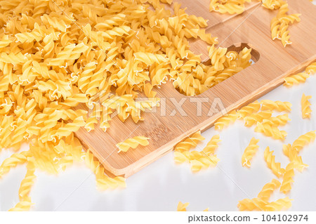 Uncooked Fusilli Pasta Scattered on Wooden Board Uncooked Fusilli Pasta Scattered on Wooden Board 104102974