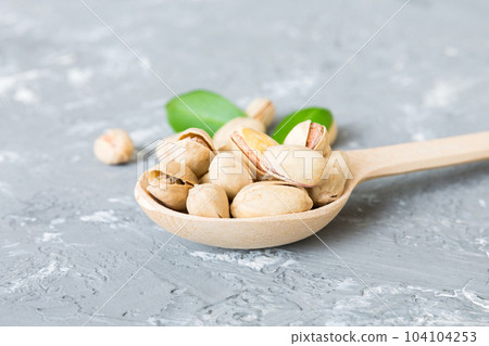 Close-up of tasty pistachio nuts in spoon with leaves on table background. Top view. Flat lay 104104253