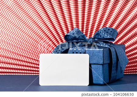 mockup card. Blue Gift box against red paper rosette. US American French flag colors. Union Jack. Happy Independence Day. Stars and stripes. Copy space. Festive paper rosette 104106630