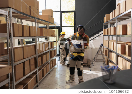 Cheerful employee having fun during storehouse inventory, listening music and dancing while analyzing merchandise checklist. Supervisor wearing protective overall preparing customers orders Cheerful employee having fun during storehouse inventory, listening music and dancing while analyzing merchandise checklist. Supervisor wearing protective overall preparing customers orders 104106682