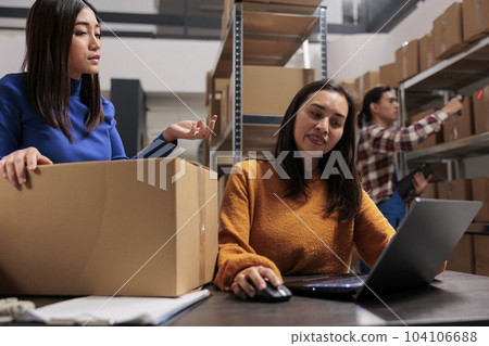 Warehouse two asian women workers planning packages delivery schedule on laptop. Business storehouse employees checking goods inventory management on computer in storage room 104106688