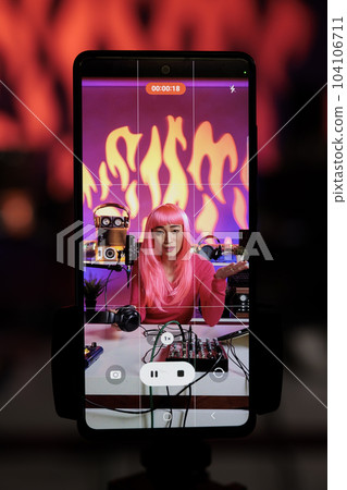 Smiling creator filming vlog using smartphone camera discussing lifestyle advice with subscribers, posting content on her channel. Asian vlogger standing in broadcast studio recording podcast Smiling creator filming vlog using smartphone camera discussing lifestyle advice with subscribers, posting content on her channel. Asian vlogger standing in broadcast studio recording podcast 104106711