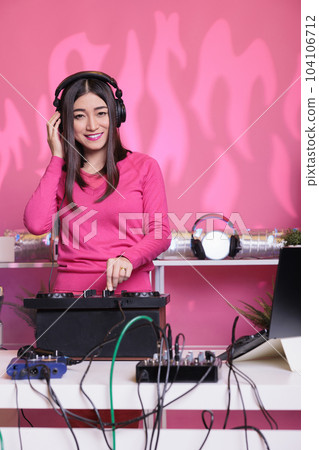 Smiling musician standing at dj table creating musical performance with remix music using professional turntables in studio. Artist performer performing techno song, enjoying nightlife in club Smiling musician standing at dj table creating musical performance with remix music using professional turntables in studio. Artist performer performing techno song, enjoying nightlife in club 104106712