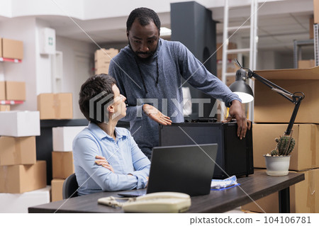 Workers discussing about metallic box while checking transportation logistics for package delivery on laptop computer. Storehouse manager analyzing online shipping order working in warehouse Workers discussing about metallic box while checking transportation logistics for package delivery on laptop computer. Storehouse manager analyzing online shipping order working in warehouse 104106781