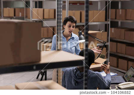 Diverse warehouse employees discussing transportation logistics problem while preparing customer packages, working in storehouse delivery department. Workers preparing online orders 104106882