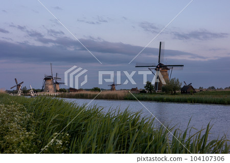 Beautiful wooden windmills at sunset in the Dutch village of Kinderdijk. Windmills run on the wind. The beautiful Dutch canals are filled with water. Beautiful sunset. Beautiful wooden windmills at sunset in the Dutch village of Kinderdijk. Windmills run on the wind. The beautiful Dutch canals are filled with water. Beautiful sunset. 104107306