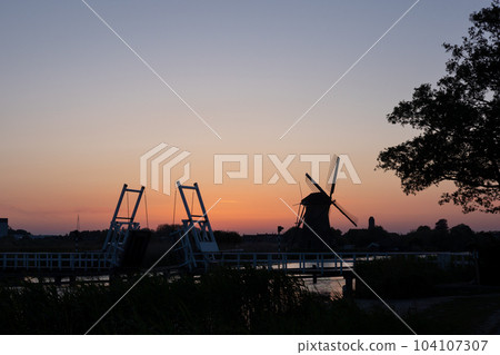 Beautiful wooden windmills at sunset in the Dutch village of Kinderdijk. Windmills run on the wind. The beautiful Dutch canals are filled with water. Beautiful sunset. Beautiful wooden windmills at sunset in the Dutch village of Kinderdijk. Windmills run on the wind. The beautiful Dutch canals are filled with water. Beautiful sunset. 104107307