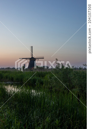 Beautiful wooden windmills at sunset in the Dutch village of Kinderdijk. Windmills run on the wind. The beautiful Dutch canals are filled with water. Beautiful sunset. Beautiful wooden windmills at sunset in the Dutch village of Kinderdijk. Windmills run on the wind. The beautiful Dutch canals are filled with water. Beautiful sunset. 104107308