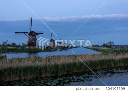 Beautiful wooden windmills at sunset in the Dutch village of Kinderdijk. Windmills run on the wind. The beautiful Dutch canals are filled with water. Beautiful sunset. Beautiful wooden windmills at sunset in the Dutch village of Kinderdijk. Windmills run on the wind. The beautiful Dutch canals are filled with water. Beautiful sunset. 104107309