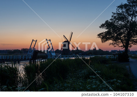 Beautiful wooden windmills at sunset in the Dutch village of Kinderdijk. Windmills run on the wind. The beautiful Dutch canals are filled with water. Beautiful sunset. Beautiful wooden windmills at sunset in the Dutch village of Kinderdijk. Windmills run on the wind. The beautiful Dutch canals are filled with water. Beautiful sunset. 104107310