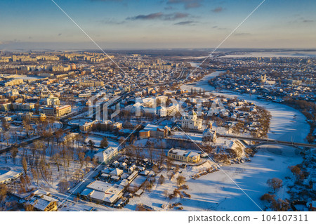 Nice top view of the winter city. Houses and buildings in the snow. Bridge over river. Orthodox churches and a Catholic cathedral. The river is covered with ice. Nice top view of the winter city. Houses and buildings in the snow. Bridge over river. Orthodox churches and a Catholic cathedral. The river is covered with ice. 104107311
