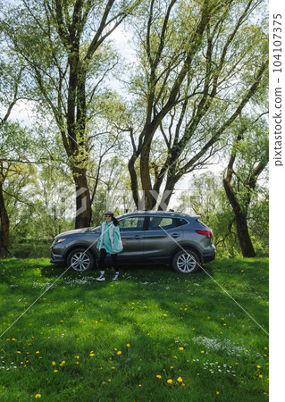a woman walks away from a parked car on a green lawn in nature a woman walks away from a parked car on a green lawn in nature 104107375