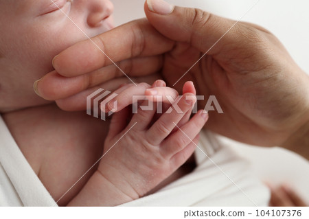 Small hand of a newborn baby with tiny fingers, head, nose and ear of a newborn. Palm hand of parents, father and mother of a newborn. Studio macro photography. Small hand of a newborn baby with tiny fingers, head, nose and ear of a newborn. Palm hand of parents, father and mother of a newborn. Studio macro photography. 104107376