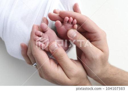 The palms of the father, the mother are holding the foot of the newborn baby on white background. Feet of the newborn on the palms of the parents. Photography of a child's toes, heels and feet. 104107383