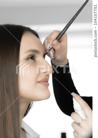 This photo shows how the eyebrow designer with care and skill creates natural and elegant eyebrows that give the client's face unsurpassed. Beautiful woman at a reception in a beauty salon 104107781